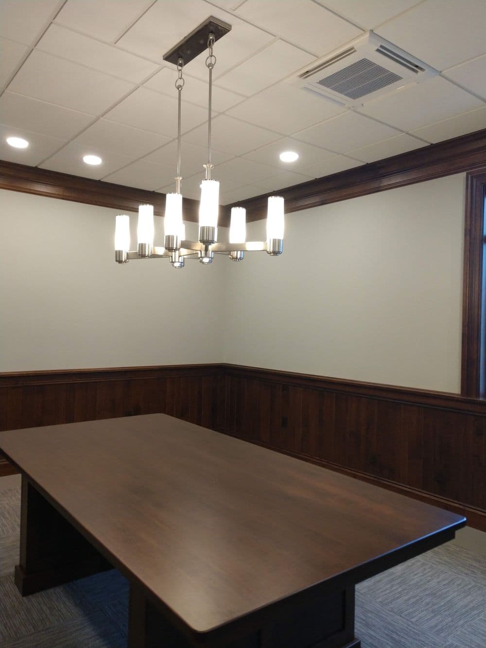 Modern conference room with wooden paneling, a large table, and stylish chandelier lighting.